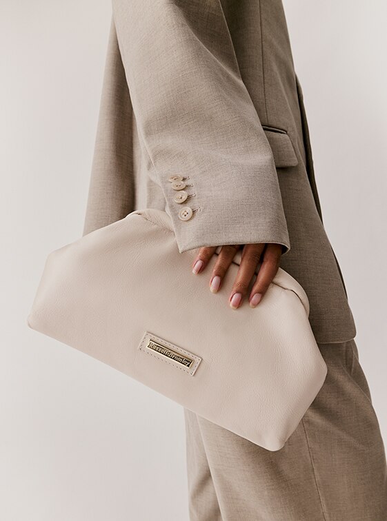 Woman holding the beige leather 'Cuddle' clutch bags by Russell and Bromley