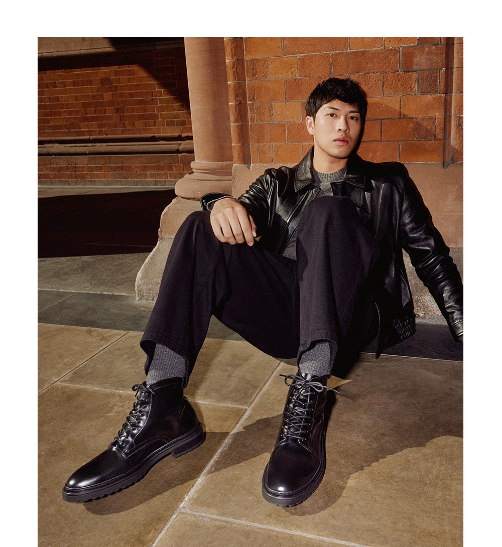 Male model sitting against the wall on train station platform wearing black leather shoes